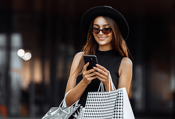 femme sur son smartphone avec des sacs de shopping