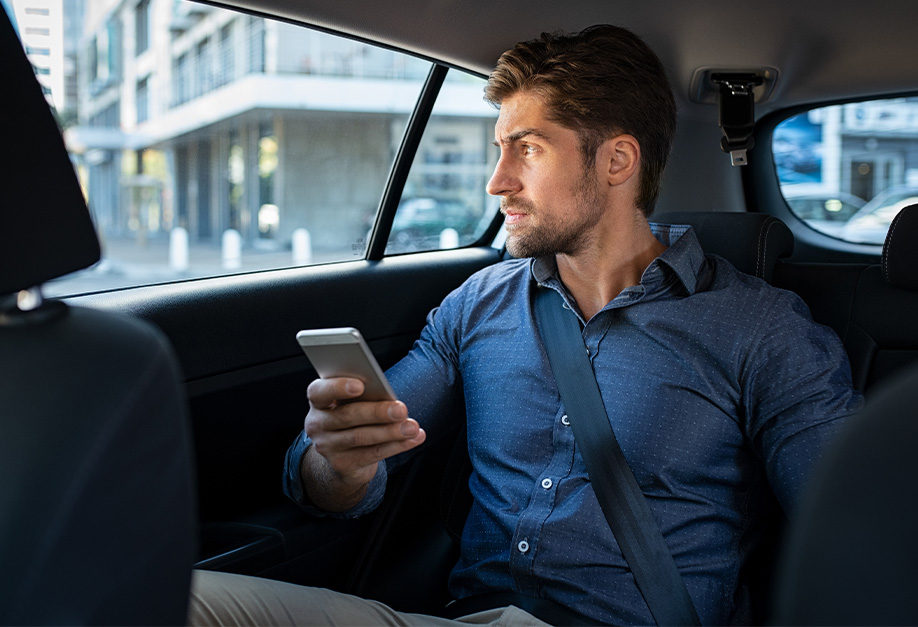 homme assis à l'arrière d'une voiture avec son smartphone à la main