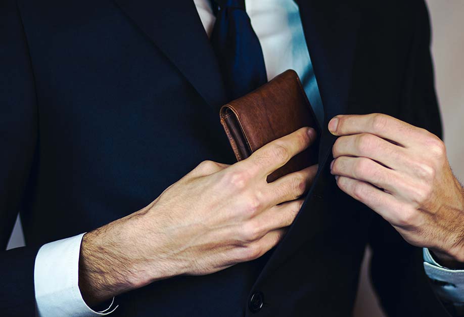 man putting his leather wallet into his suit pocket